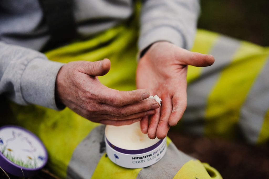 Hand applying organic tallow skincare cream outdoors, eco-friendly beauty product.