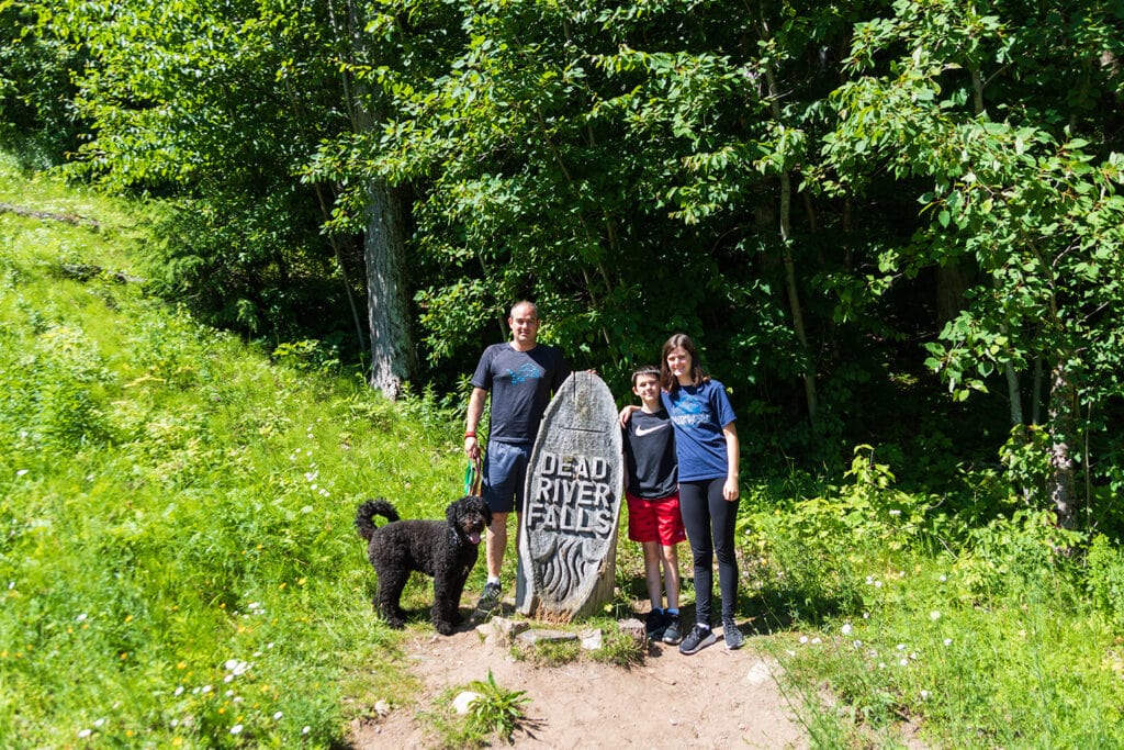 Explore the Natural Beauty of Dead River Falls In Marquette Dead River Falls trail marker. It looks like an old tree trunk that's been shaped into an oval and has dead river falls carved into it.