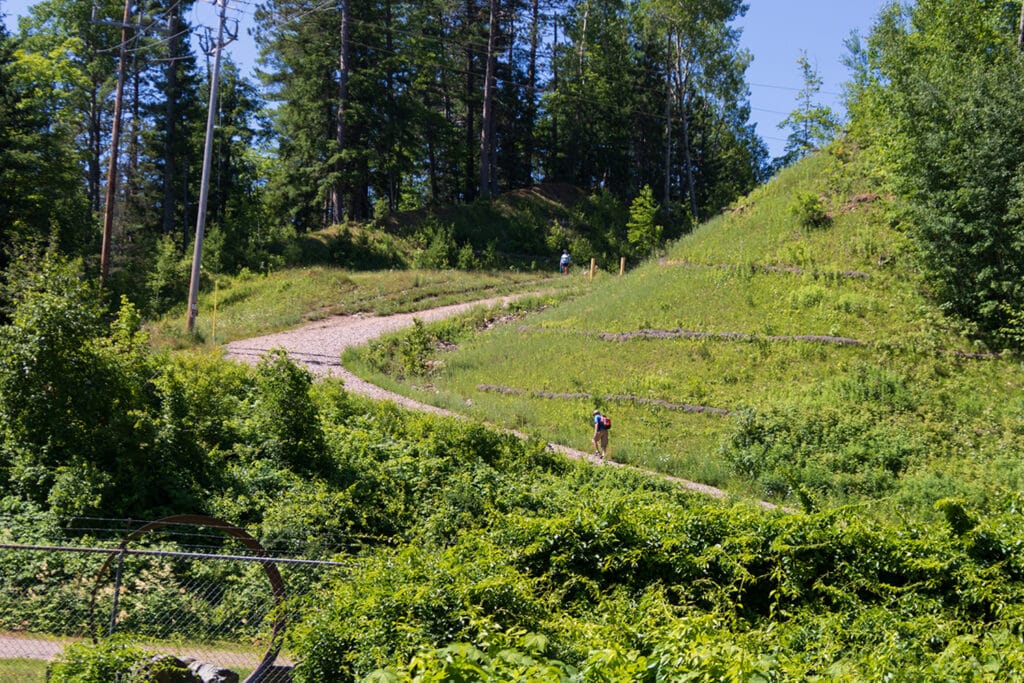 Explore the Natural Beauty of Dead River Falls In Marquette The start of Dead River Falls trail. It's a picture of a steep, gravel, access road surrounded by lush forest.