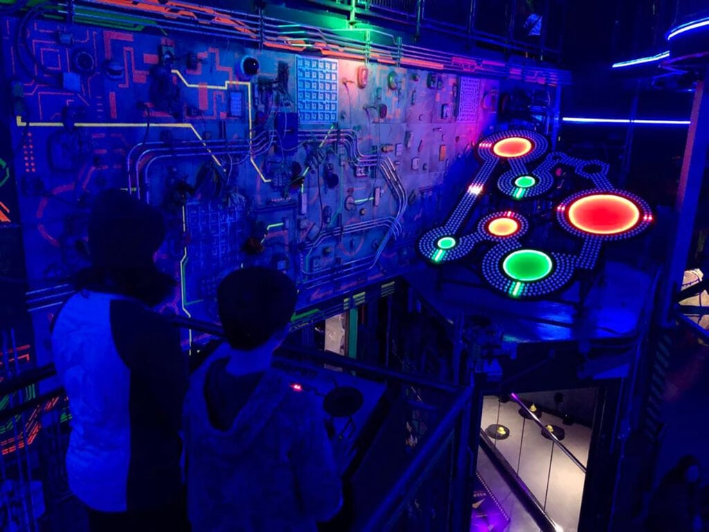 Meow Wolf’s Omega Mart Las Vegas | Ultimate Guide A dark industrial arcade-style room of Omega Mart lit up by bright colorful lights.