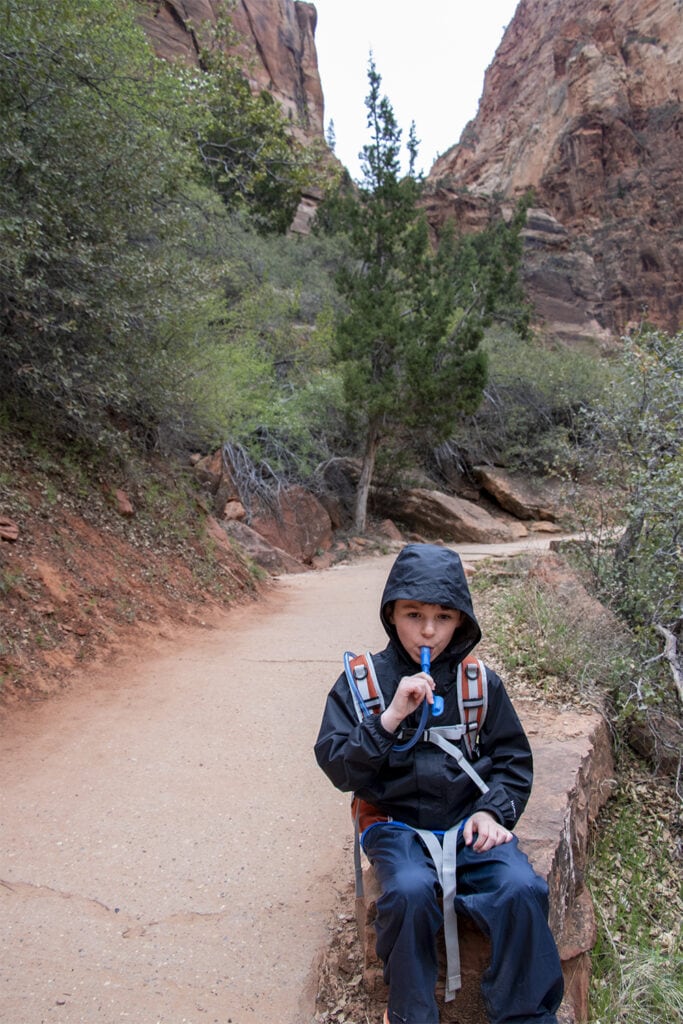 What to Pack for Zion National Park: A family-friendly Guide Young child staying hydrated during a hike in Zion National Park, taking a drink from his hydration backpack.