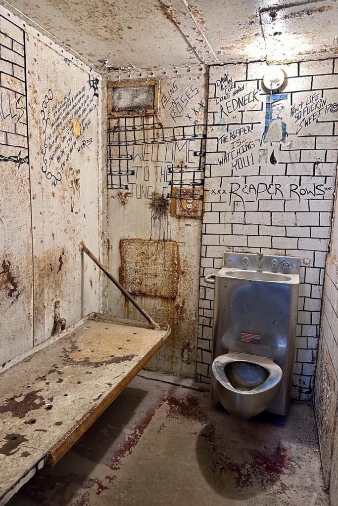 West Virginia Penitentiary: Family Tours Guide 2025 Small prison cell with writing covering the interior walls inside the penitentiary
