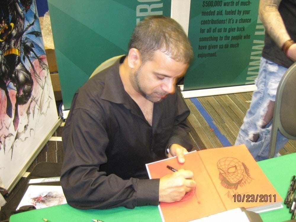 Artist signing artwork at Hero Initiative event for charity and comic book industry support.