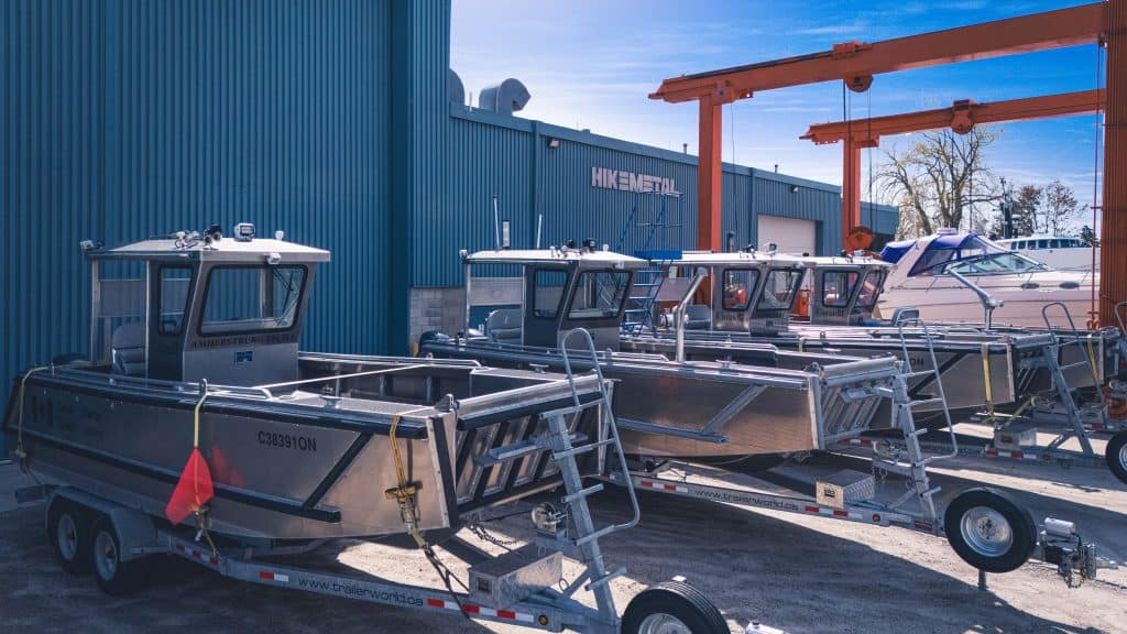 Multiple aluminium boats on trailers outside a boat manufacturing facility.