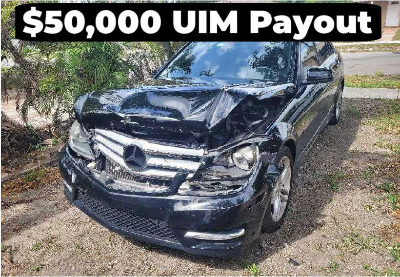 Damaged black Mercedes-Benz with crushed front end after crash, caption reads '$50,000 UIM Payout