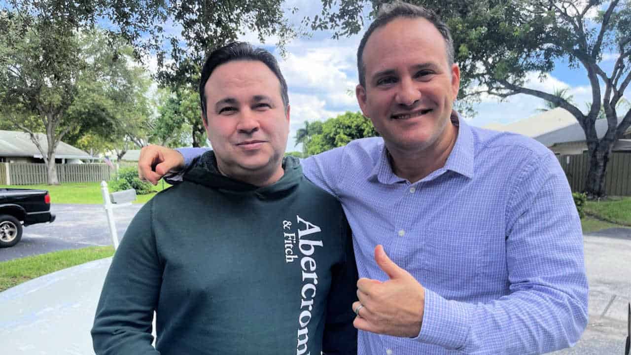 Injury lawyer Justin Ziegler smiling with his client outside after successfully settling his personal injury case. The client stands next to him, looking content. Trees and a residential neighborhood are visible in the background.