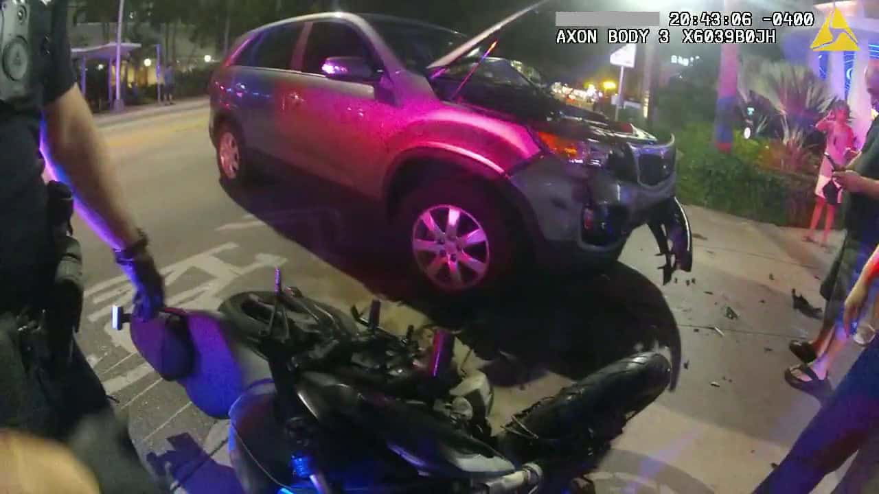 Accident scene showing a motorcycle and a damaged car after a collision. Emergency responders are pr.