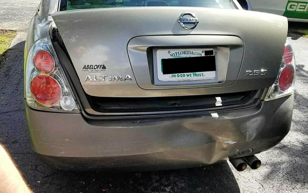 Rear view of a silver Nissan Altima sedan with visible damage to the rear bumper;  