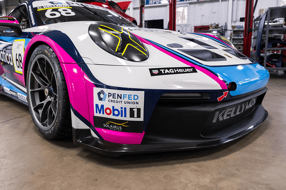 Race-ready Porsche 911 Cup Car 992 with vibrant pink and blue livery in garage.
