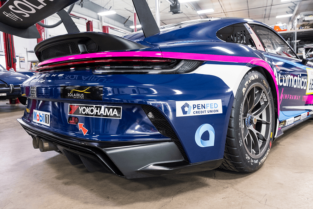 Blue Porsche 911 Cup Car with racing decals and pink stripe in garage.