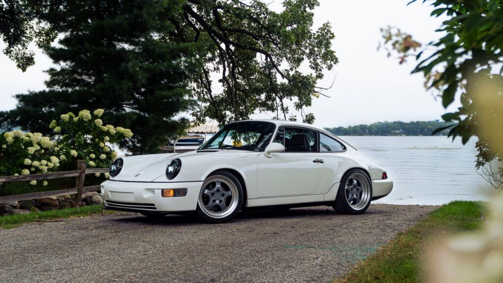 Classic white 1993 Porsche 964 parked near a lake with trees in the background.
