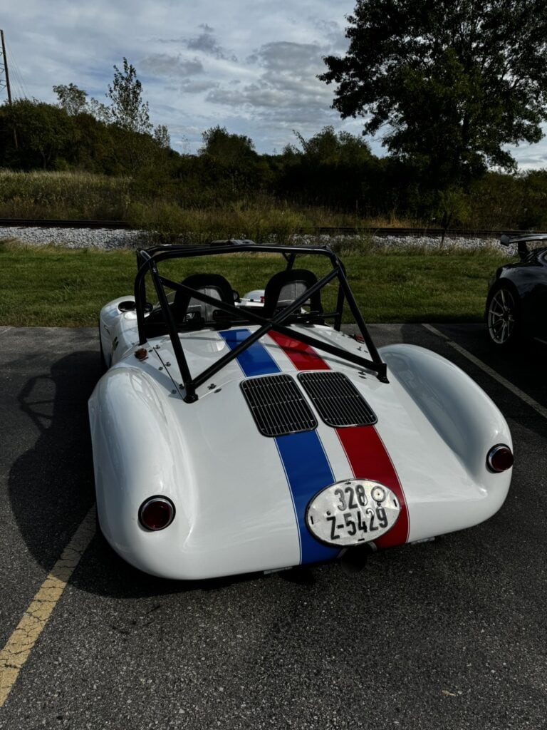 White 1966 Porsche 550 Spyder with racing stripes in a parking lot.