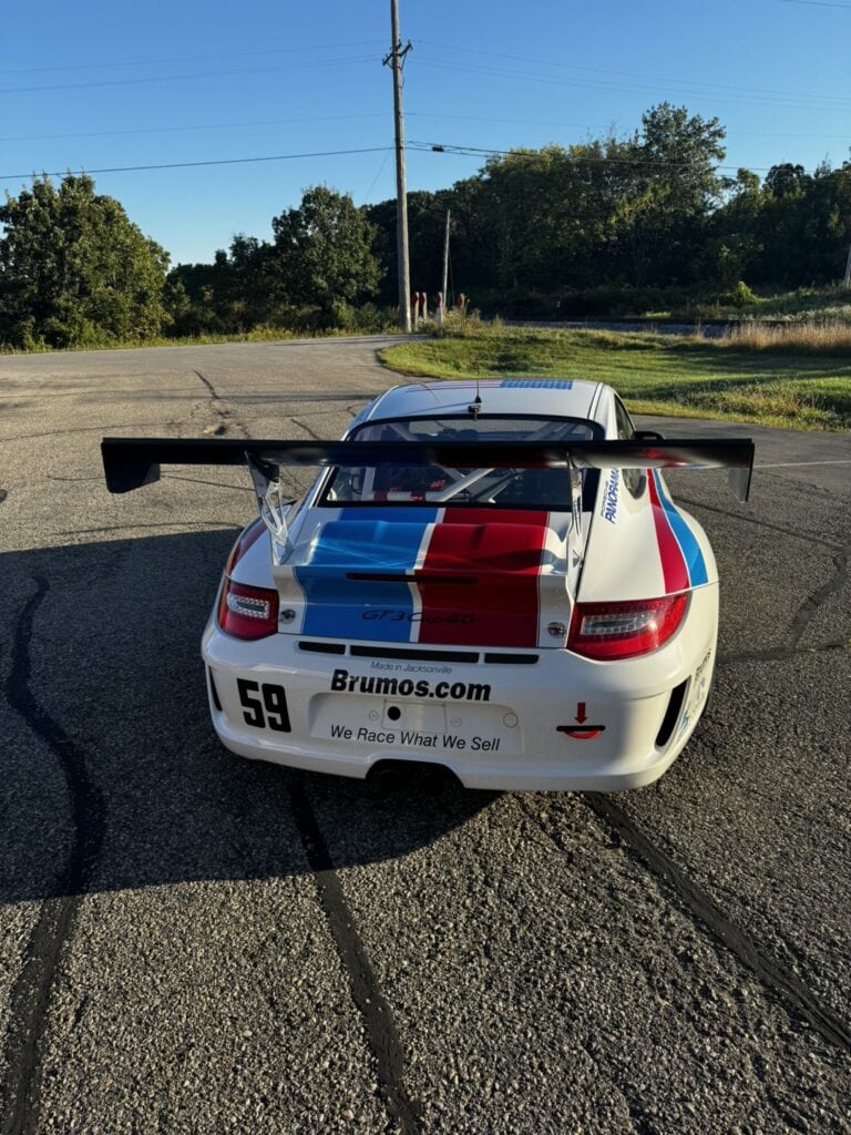 White Porsche 997 Cup race car with red and blue stripes and large rear wing.