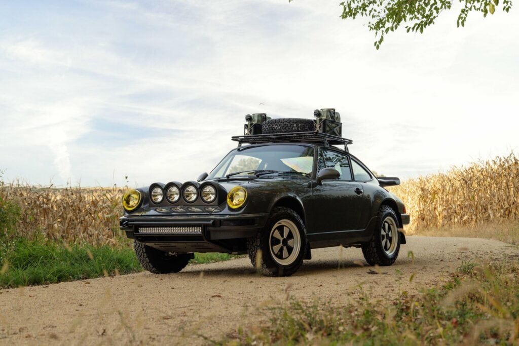 Black Porsche 964 with off-road gear in rural landscape.