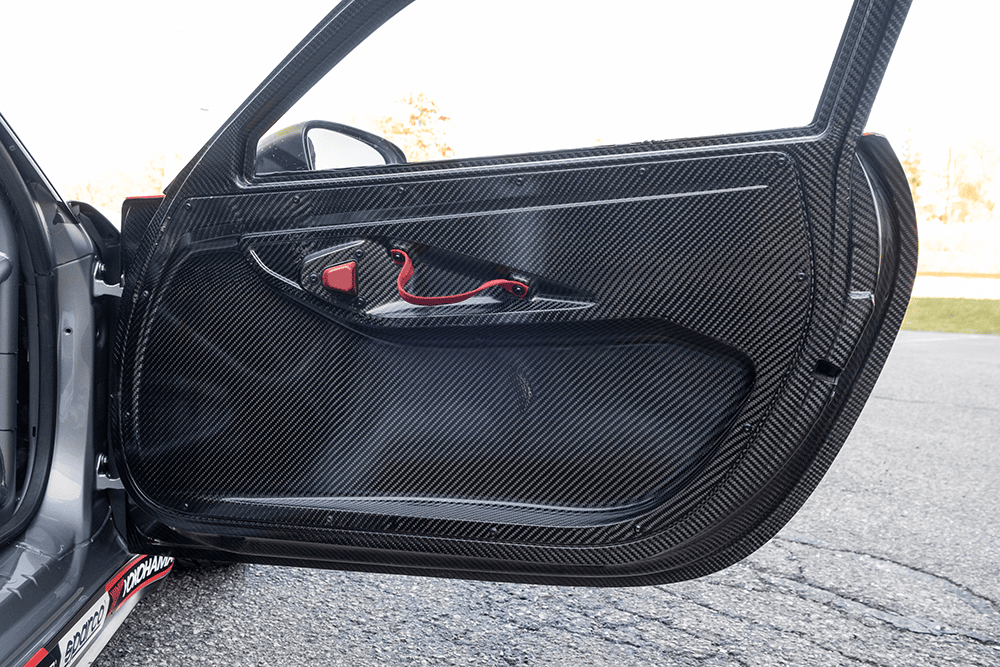 Close-up of a carbon fiber car door panel with red safety latch.