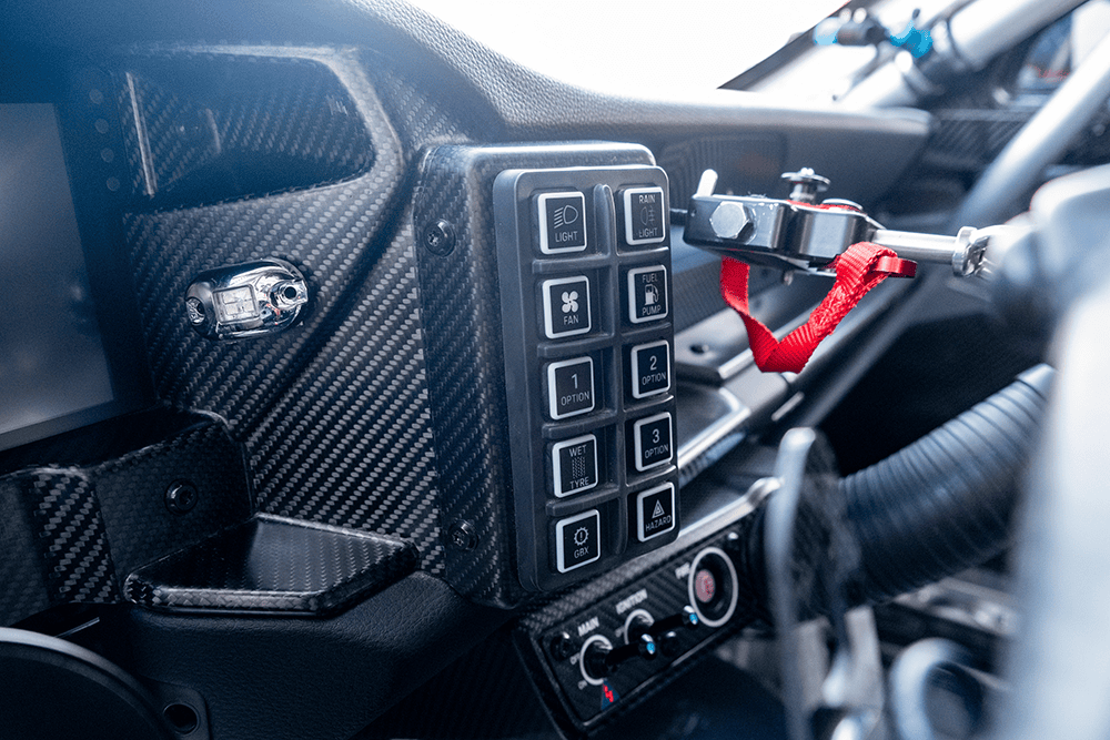 Close-up of race car dashboard with switches and steering wheel.