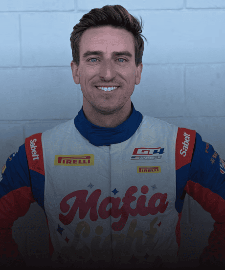 Race car driver in racing suit smiling at the camera during Pirelli GT4 America event.