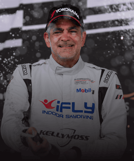 Race car driver celebrating on podium after Porsche Carrera Cup North America race.