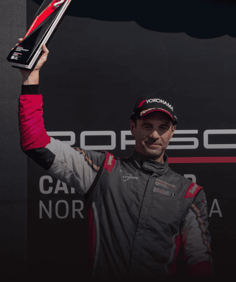 Race car driver holding trophy at Porsche Carrera Cup North America event.