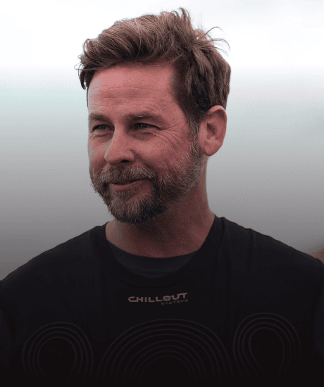 Man with brown hair and beard smiling outdoors during daytime.