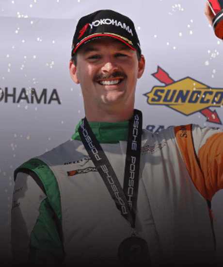 Race car driver celebrating on podium at Porsche Sprint Challenge event.