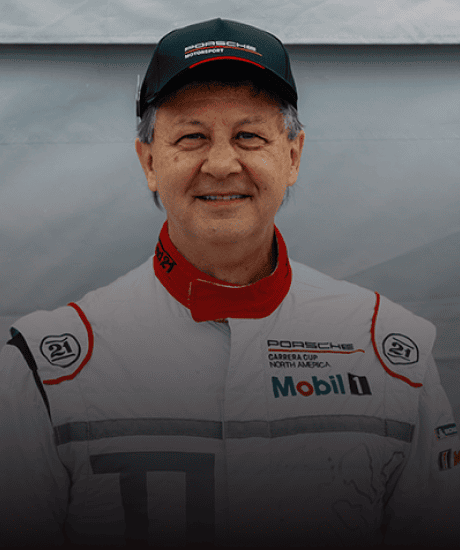 Porsche race car driver in racing suit and cap at Porsche Club of America event.