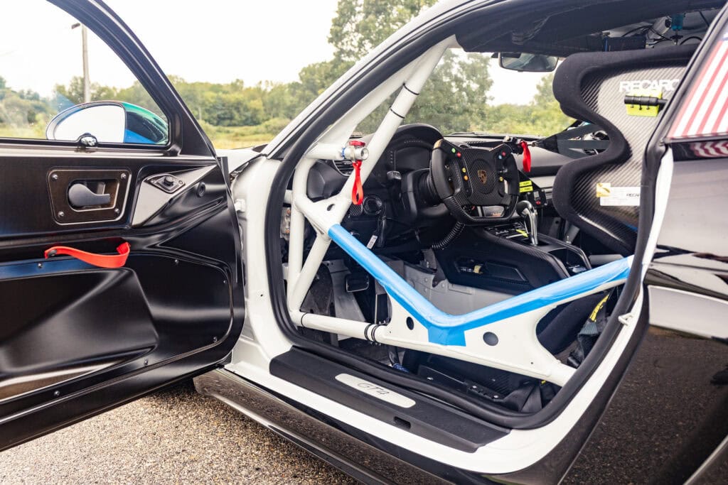 Race car interior with racing seat, steering wheel, and safety roll cage.