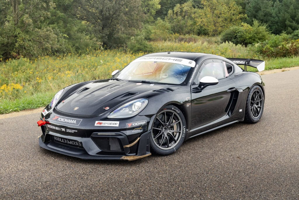 Black Porsche 718 Cayman GT4 RS with racing decals on a road.