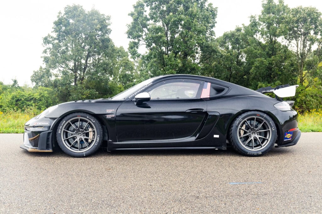 Black Porsche 2025 GT4 Clubsport RS on road with trees in background.