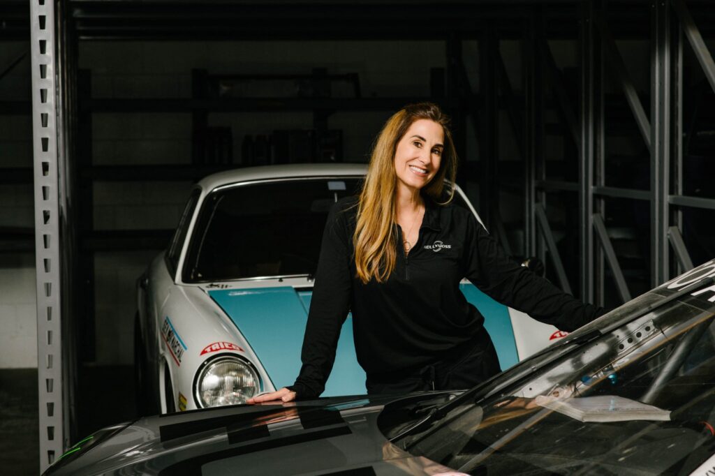 Kellymoss team member smiling in garage with race cars.