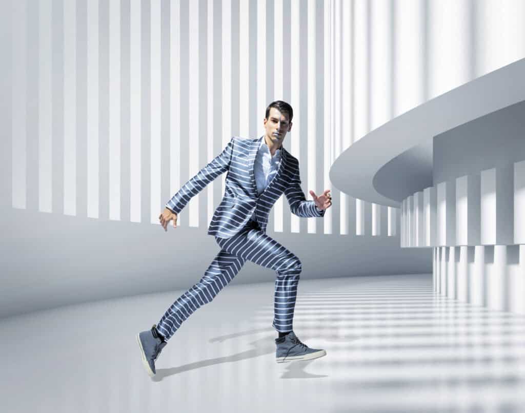 Man in a stylish striped suit walking confidently in a sleek, modern architectural environment.
