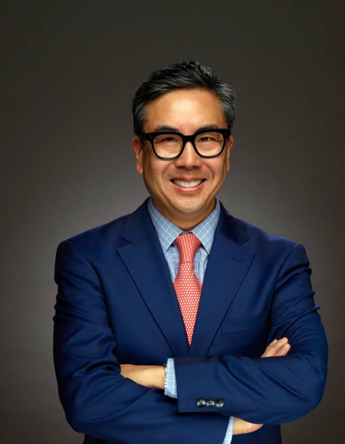 Confident professional man in formal suit with glasses smiling, arms crossed.