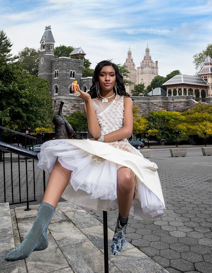 Fashion model in fairy tale-inspired white dress with cityscape background.