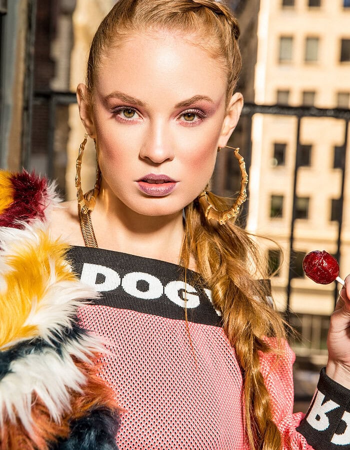 Fashion model with braided hair and bold makeup outdoors in city setting.
