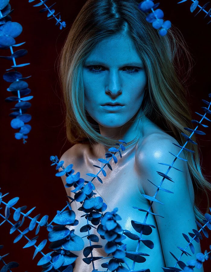 Fashion portrait of a woman with blue lighting and eucalyptus leaves. photographer NYC