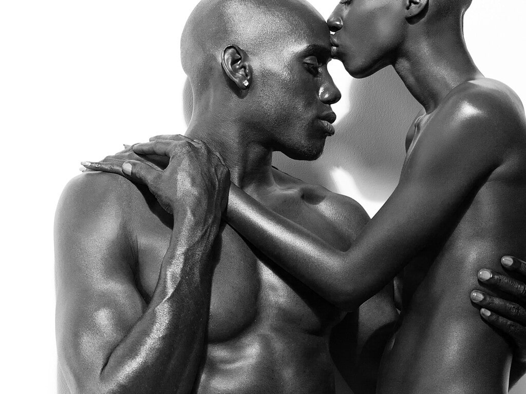 Closely cropped black-and-white portrait of two models holding one another.