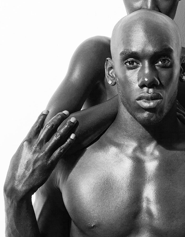 Male model facing the camera while a female model poses behind him in a black-and-white portrait.