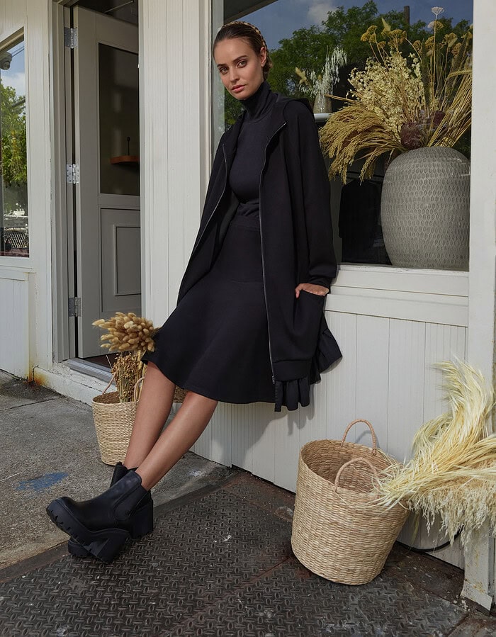 Fashionable woman in black coat and dress sitting outside storefront. photographer NYC