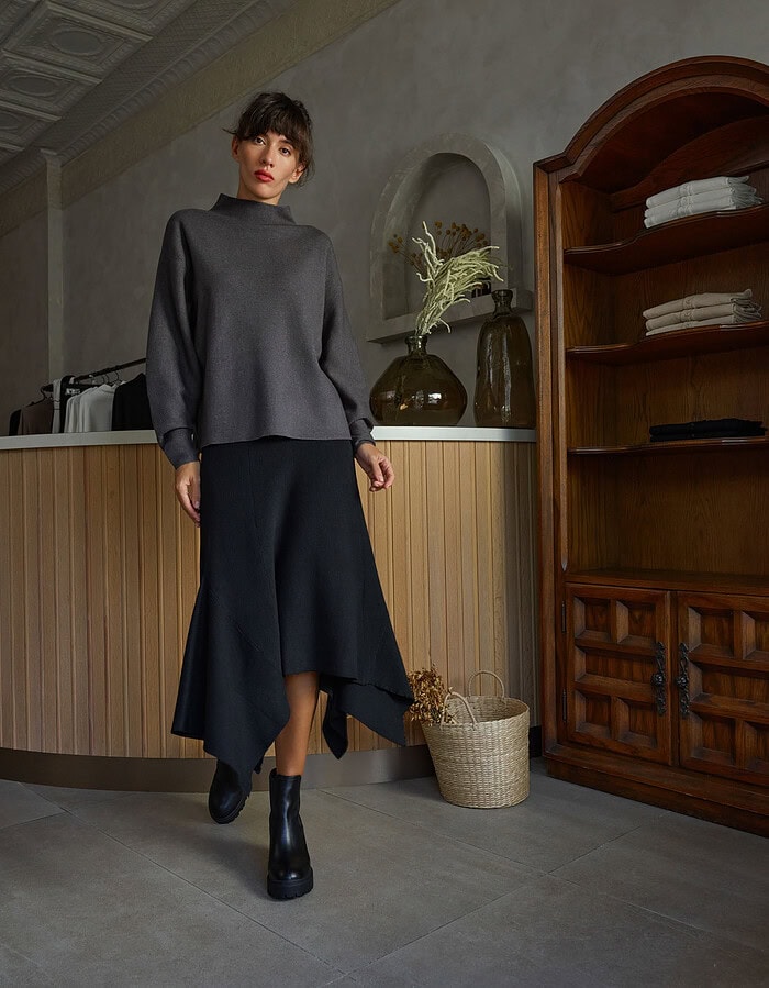 Fashionable woman in dark gray sweater and asymmetrical skirt in stylish interior. photographer NYC