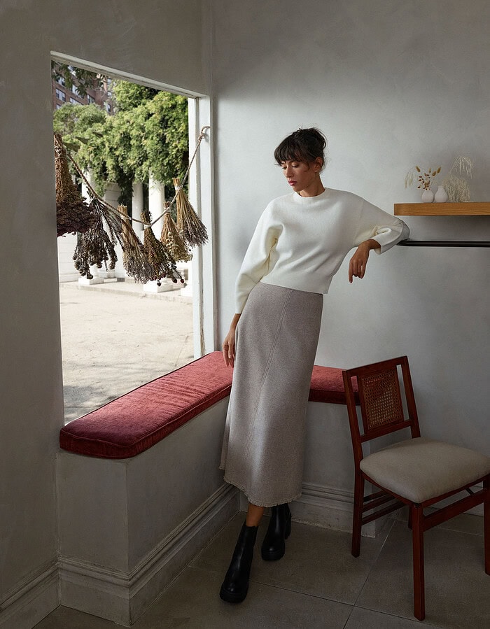 Fashionable woman in a white sweater and gray skirt indoors near a window. photographer NYC