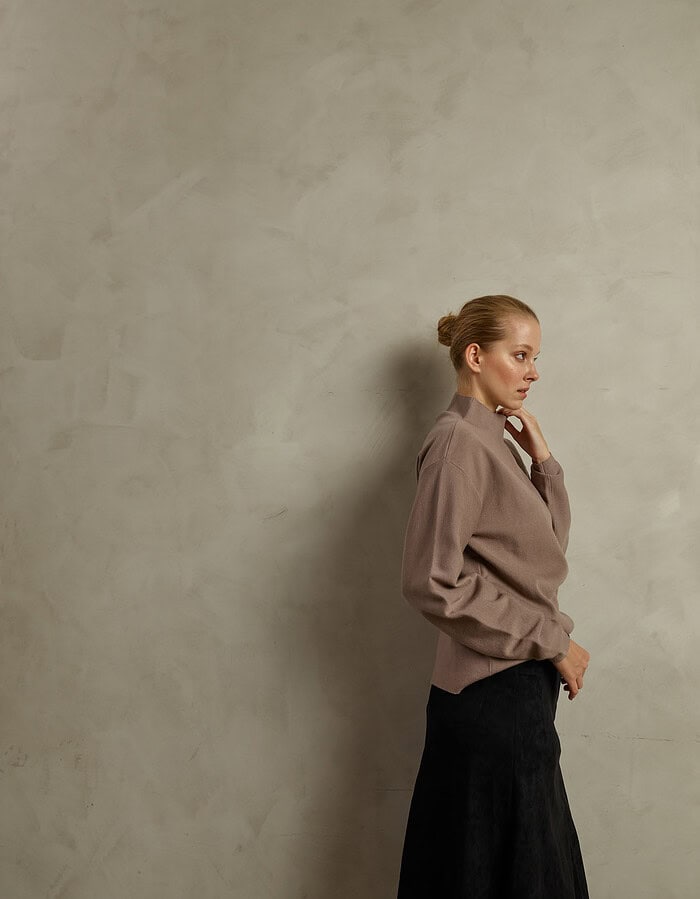Elegant woman in beige jacket and black skirt standing against a textured wall. photographer NYC