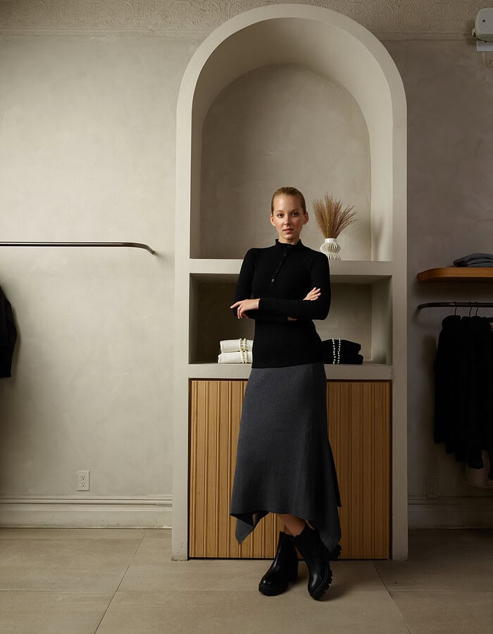 Elegant woman in black top and gray skirt standing in modern interior. photographer NYC