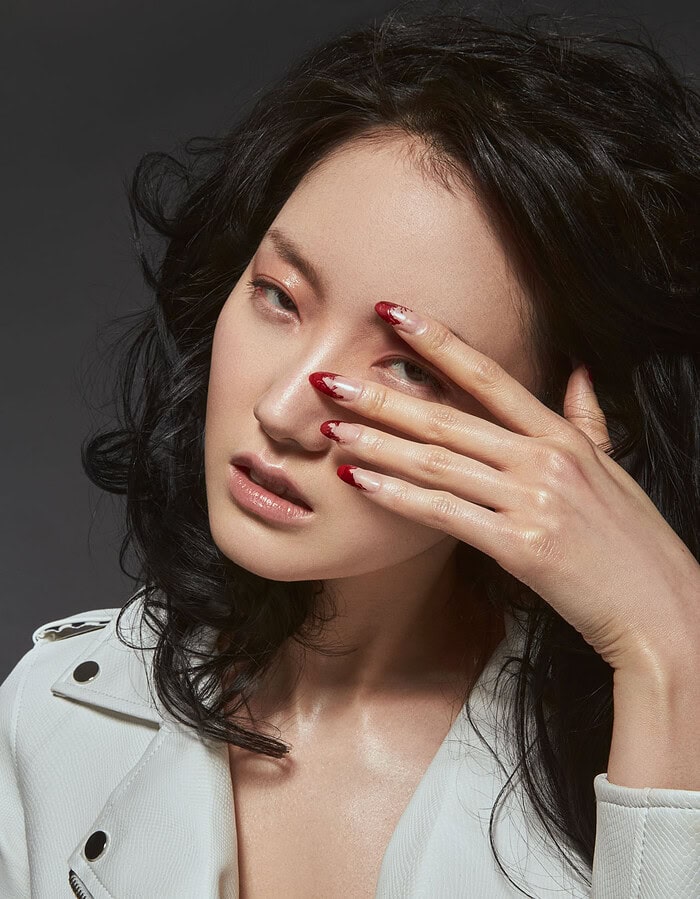 Portrait of a woman with dark hair and red nails covering one eye. photographer NYC
