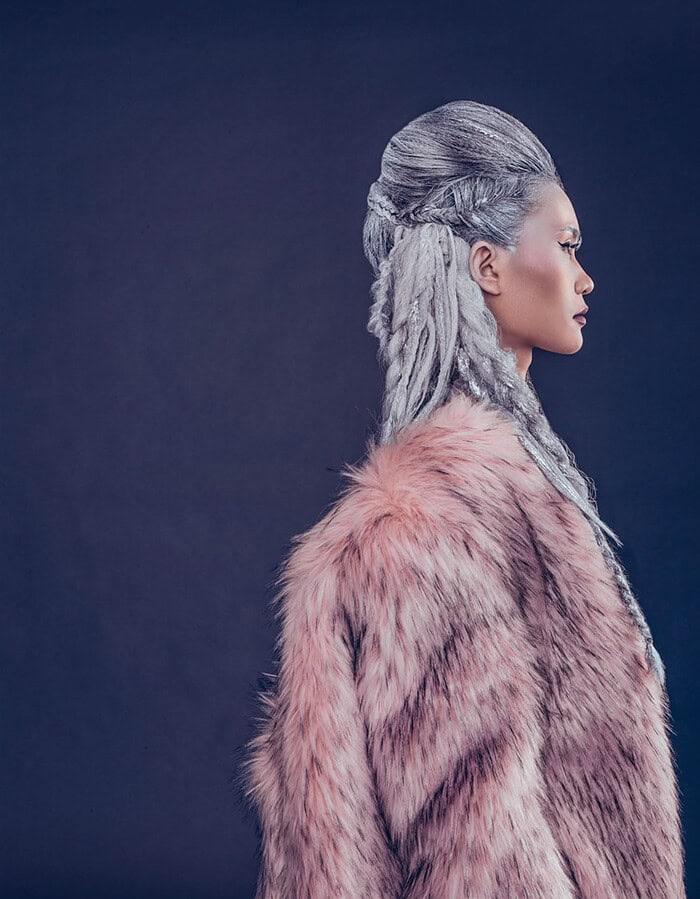 Profile portrait of a fashion model with silver braided hair wearing a soft pink fur coat.