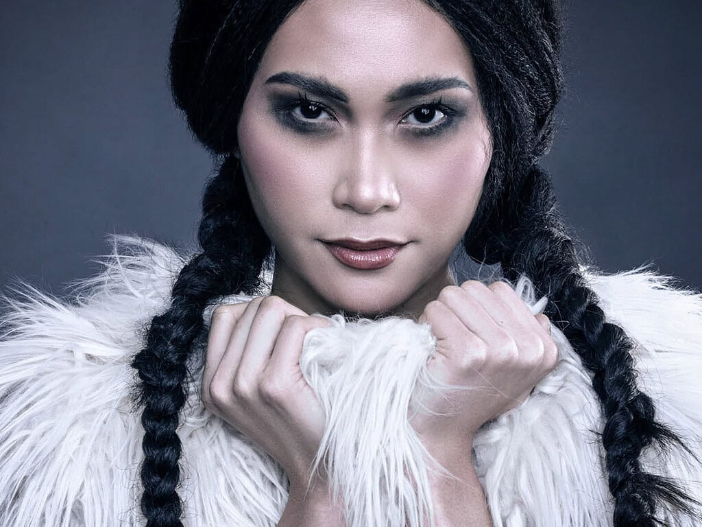Close-up beauty portrait of a model with black braids holding a white shaggy fur garment beneath her face.