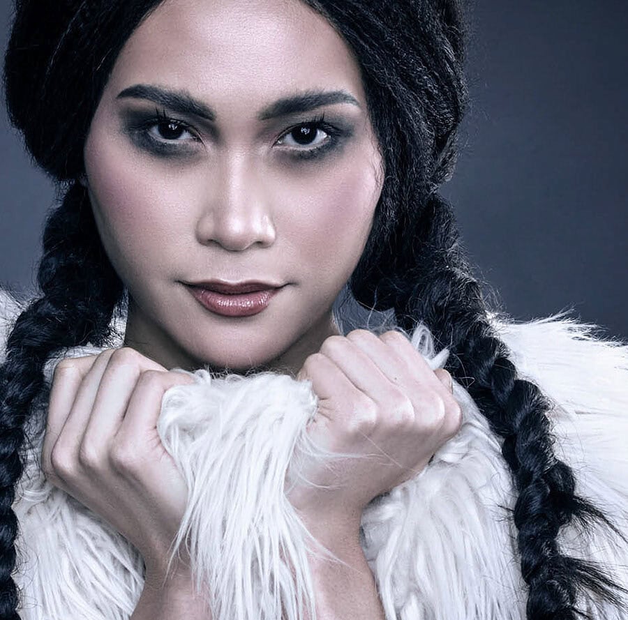 Close-up beauty portrait of a model with black braids holding a white shaggy fur garment beneath her face.