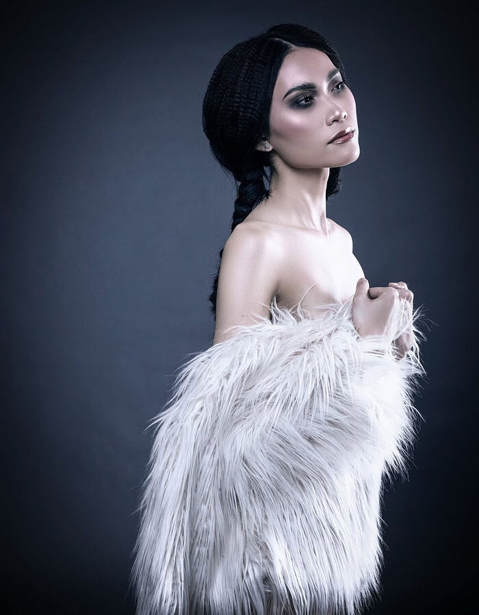 Side-profile fashion portrait of a model with black braids wearing a white shaggy fur wrap.