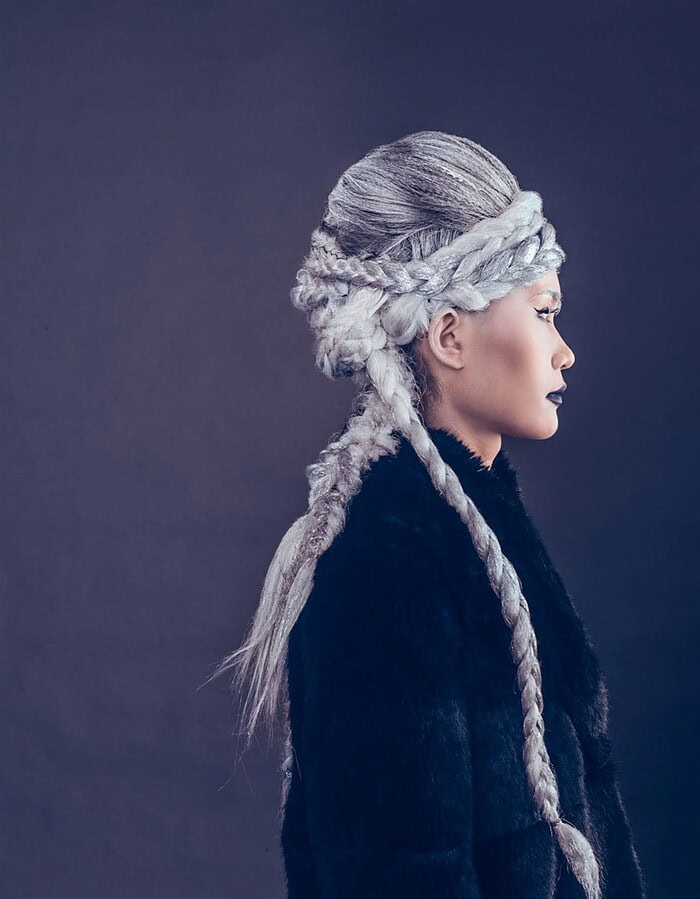 Profile portrait of a fashion model with an elaborate silver braided hairstyle wearing a black fur coat.