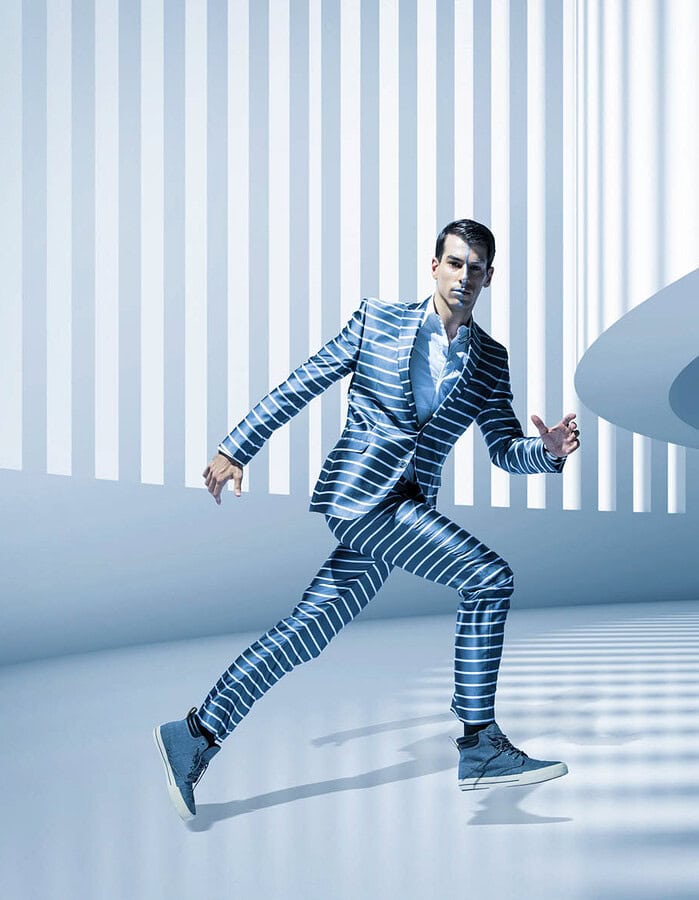 Male fashion model in a blue striped suit posing dynamically inside a futuristic white architectural environment.