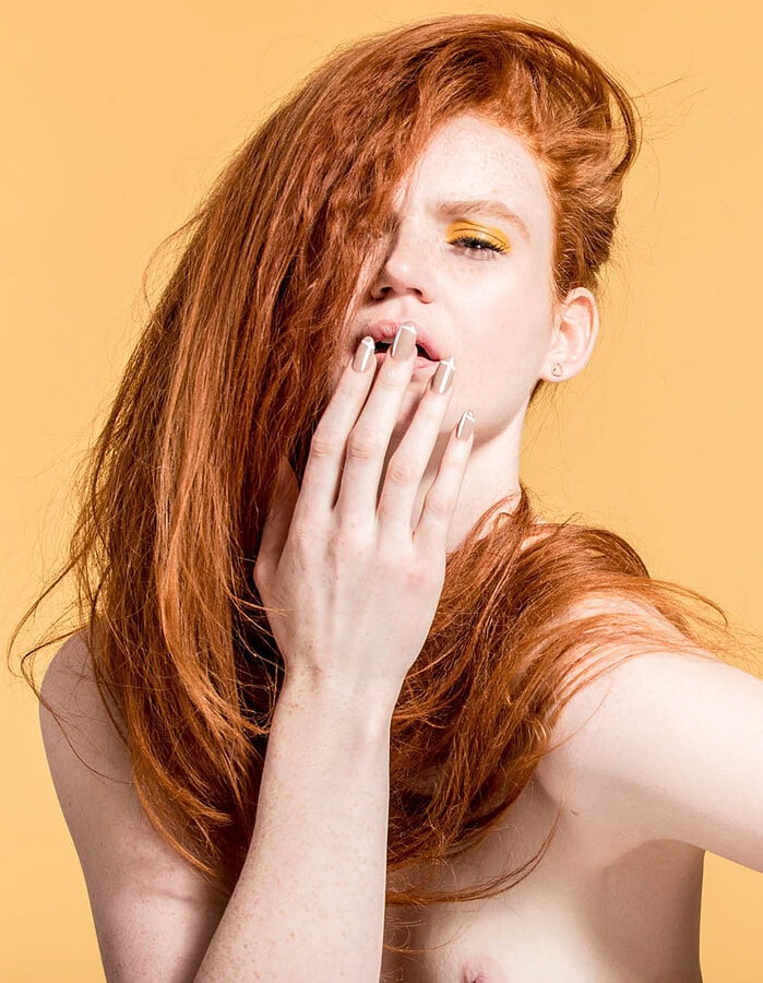 Close horizontal beauty portrait of a red-haired model with her hand resting near her lips.